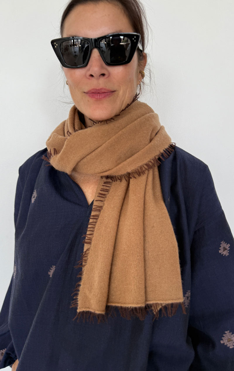 Person wearing a brown scarf and dark sunglasses against a white background