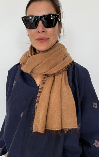 Person wearing a brown scarf and dark sunglasses against a white background