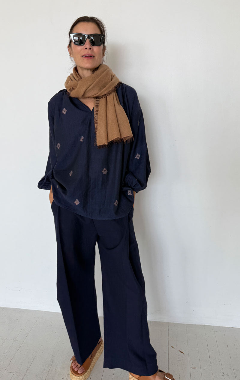 Person wearing a navy outfit with a brown scarf against a white background